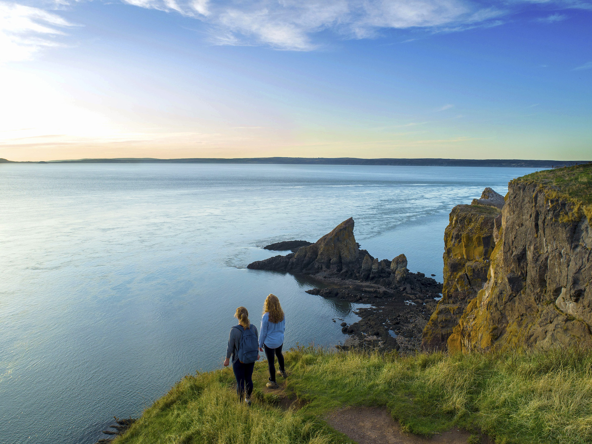 Two women standing on a cliff at Cape Split overlooking the ocean.