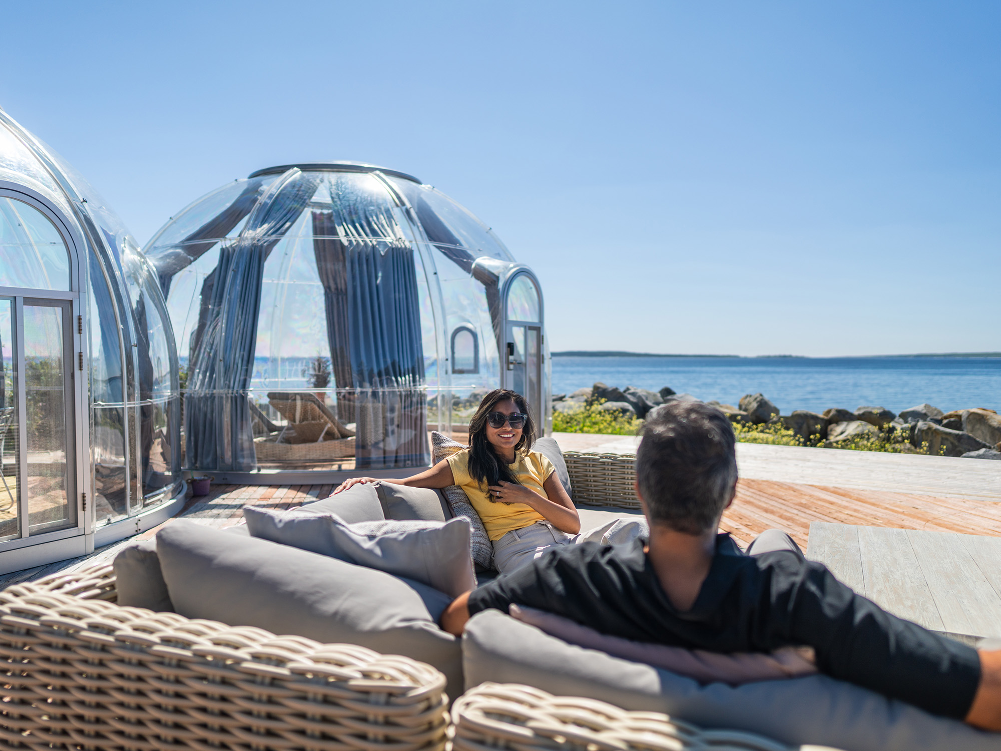 The owners and operators of Sidanna Retreat sitting on patio furniture with a clear climate controlled weatherproof dome in the background.